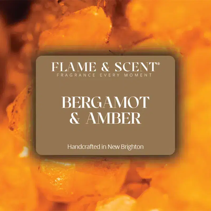 BA Flame & Scent A label reads Flame & Scent Fragrance Every Moment. Bergamot & Amber Candle, hand-crafted in New Brighton, sits before a blurred background of warm amber crystals.
