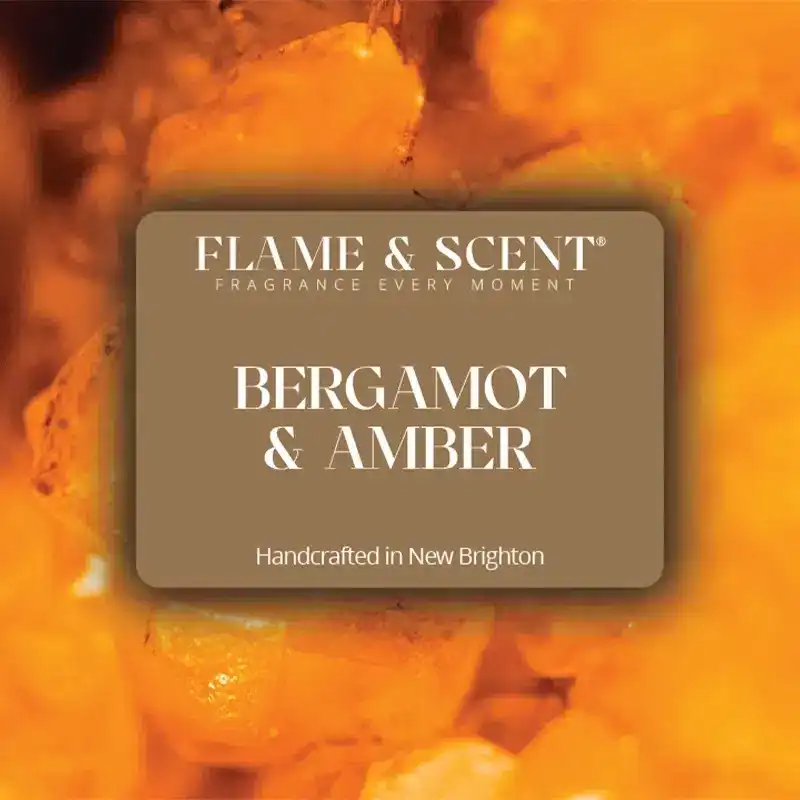 Flame & Scent A label reads Flame & Scent Fragrance Every Moment. Bergamot & Amber Candle, hand-crafted in New Brighton, sits before a blurred background of warm amber crystals.
